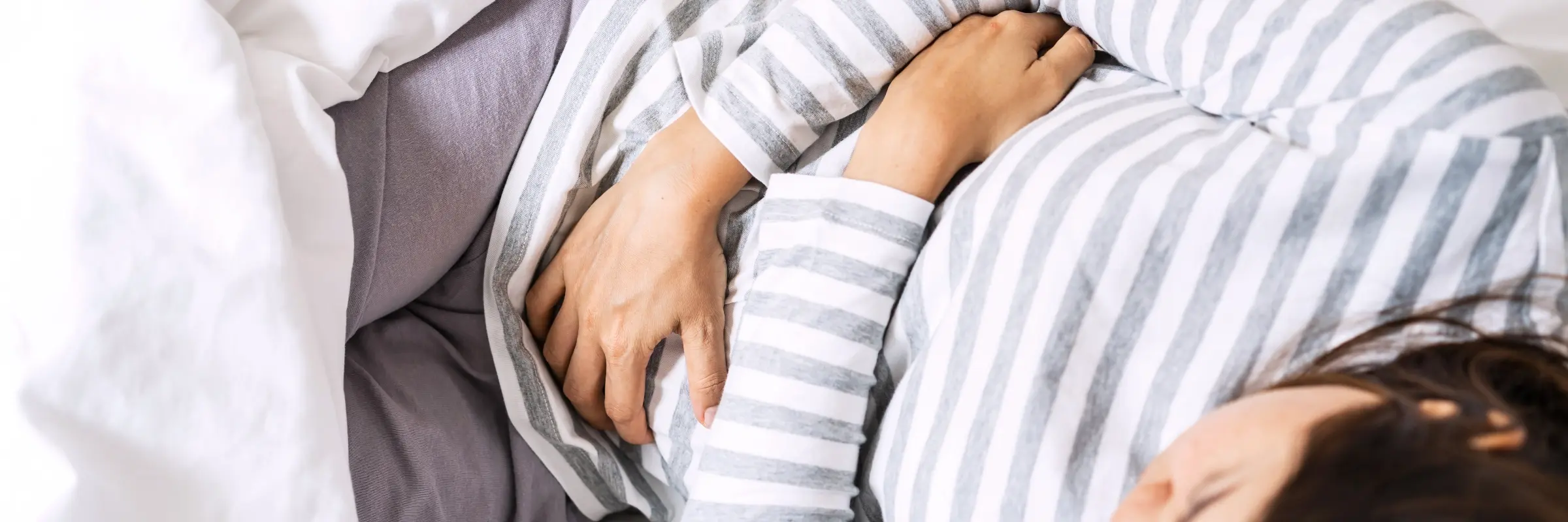 Frau liegt zusammengerollt im Bett und drückt die Hand auf den Unterbauch – Akupunktur bei Menstruationsbeschwerden