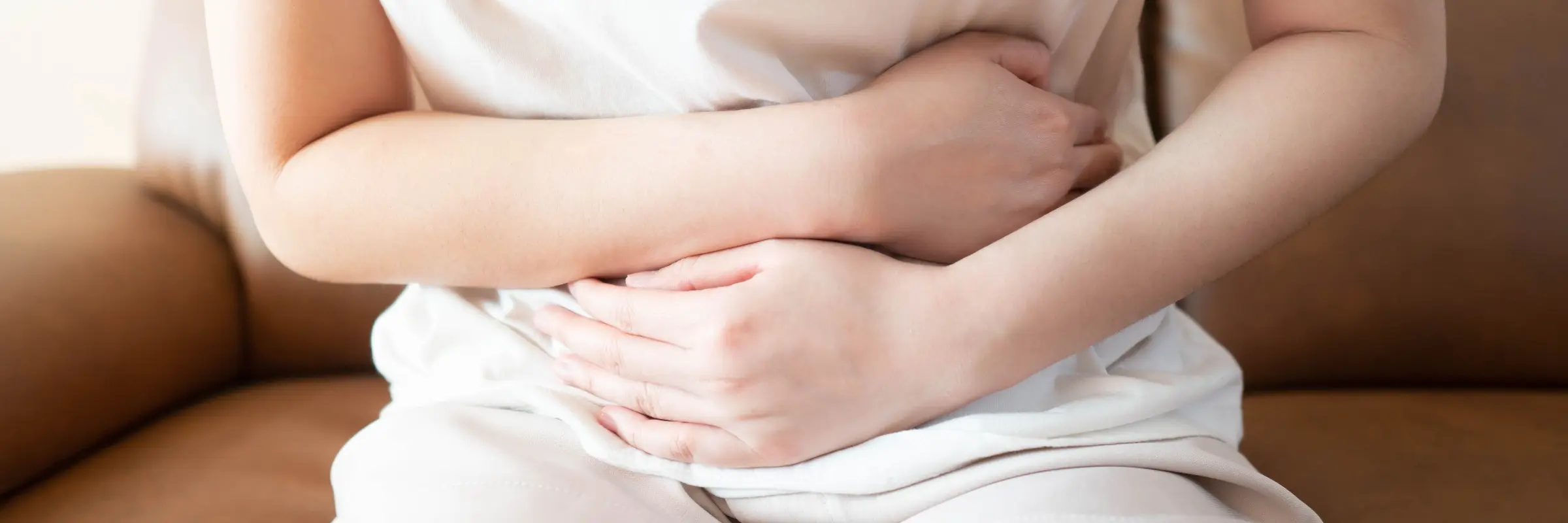 Frau liegt mit angezogenen Beinen im Bett und drückt beide Hände auf den Bauch – Akupunktur bei Reizdarm